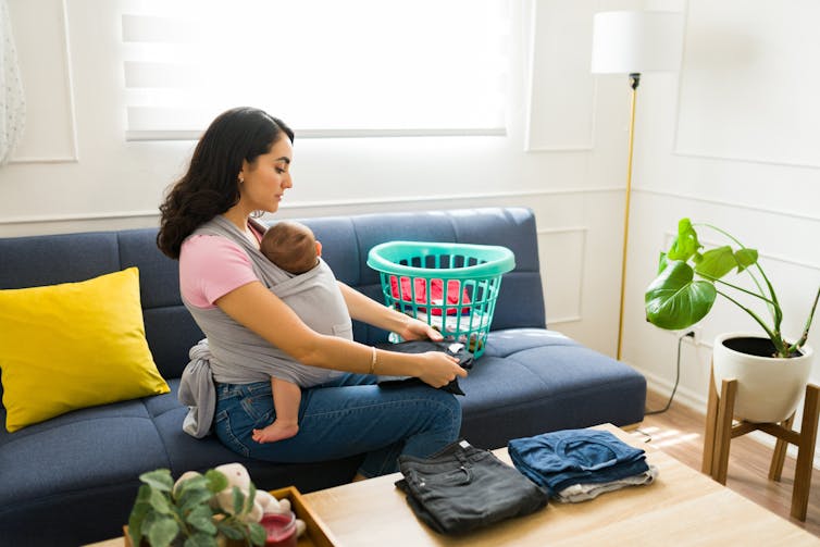 A woman with a baby in a carrier on her front folds washing