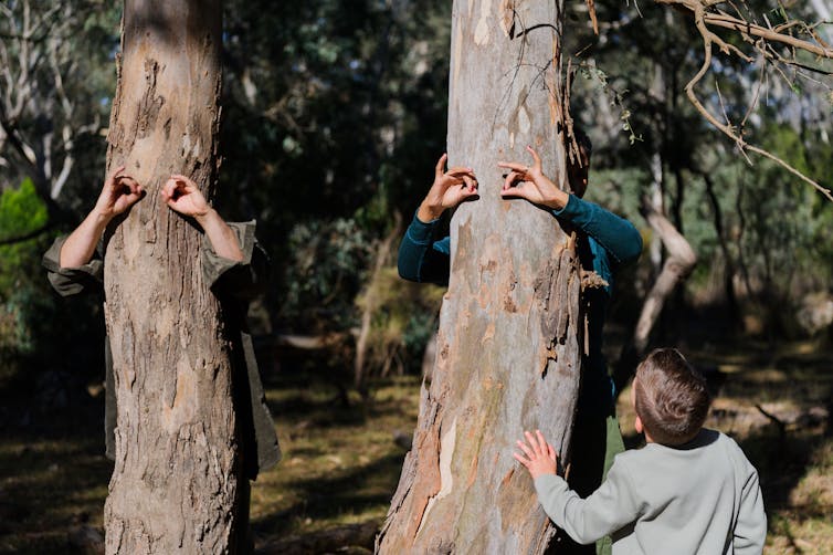 Children stand behind trees and make eyes with their hands.